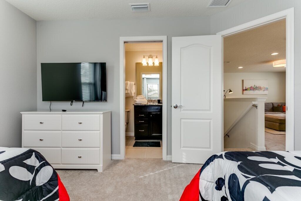 A bedroom with a TV, white dresser, and a door leading to a bathroom.
