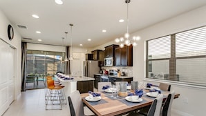A modern kitchen with dark cabinets, a wooden dining table set for four, and a large window with blinds. - 5 BED 5 Bath Resort Villa (Kissimmee)