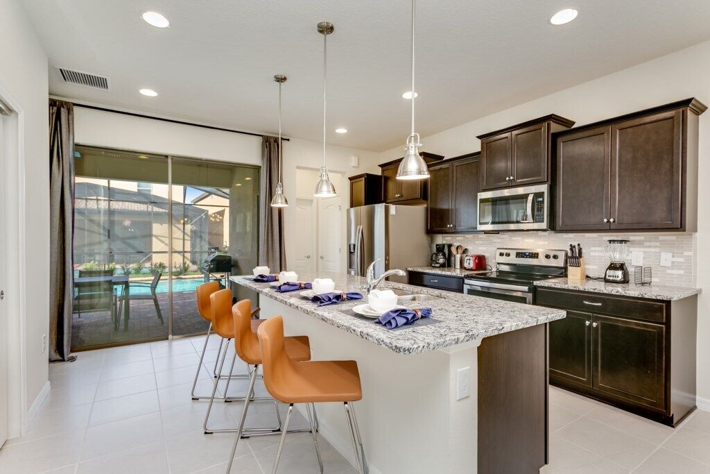 A modern kitchen with dark cabinets, a central island with bar stools, and a large window overlooking a pool.