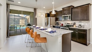 A modern kitchen with dark cabinets, a central island with bar stools, and a large window overlooking a pool. - 5 BED 5 Bath Resort Villa (Kissimmee)