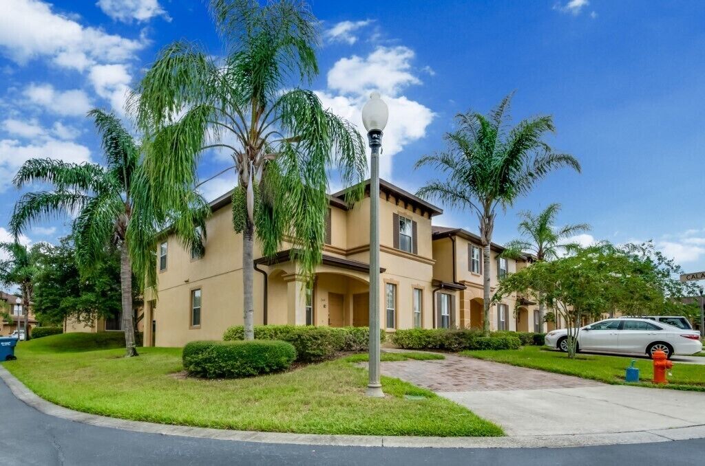 Un edificio residencial de varios pisos con fachada color beige, rodeado de céspedes cuidados y palmeras.