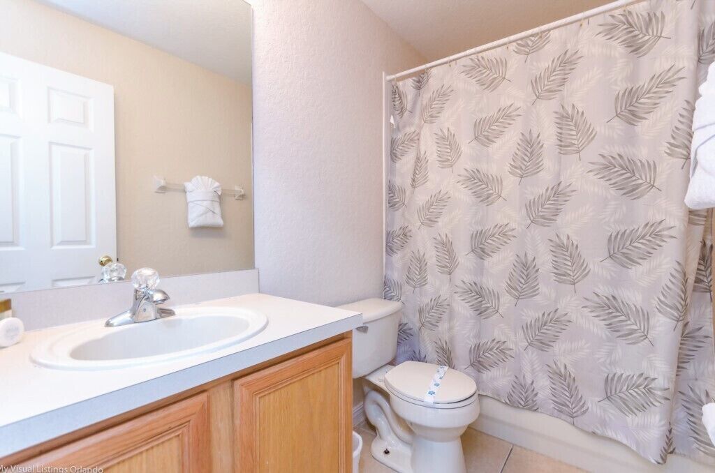 A bathroom with a white sink, a toilet, and a shower curtain with a leaf pattern.