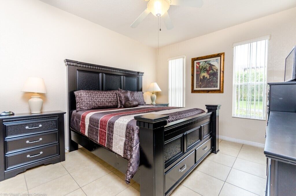 Een slaapkamer met een bed, nachtkastjes, een dressoir en een plafondventilator.