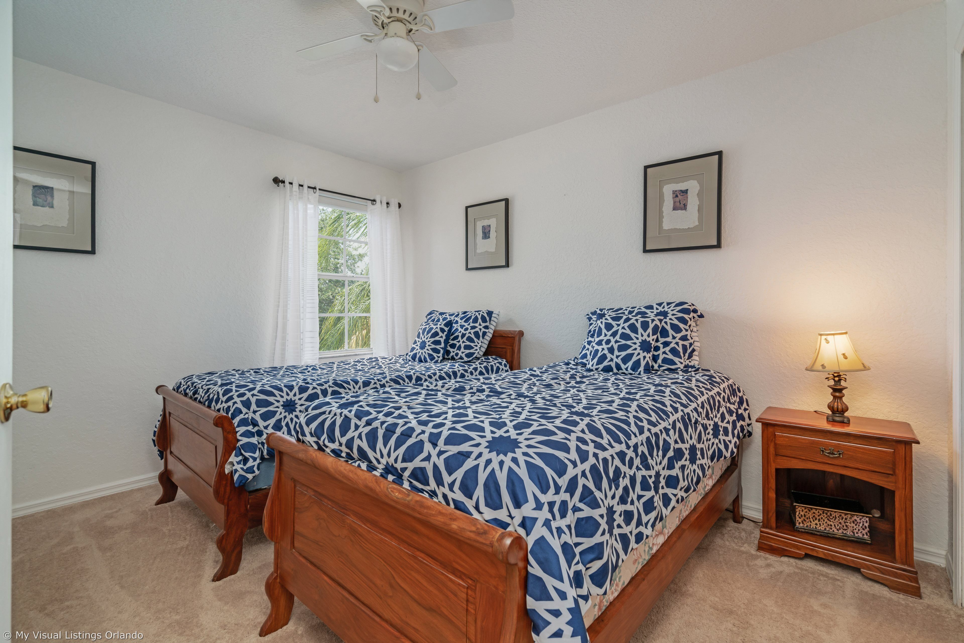 A bedroom with two wooden beds, a nightstand with a lamp, and framed pictures on the walls.