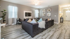 A modern living room with a grey sofa, a flat-screen TV, and a dining area with a white table and chairs. - 9044st00 Premium-lot Location (Davenport)