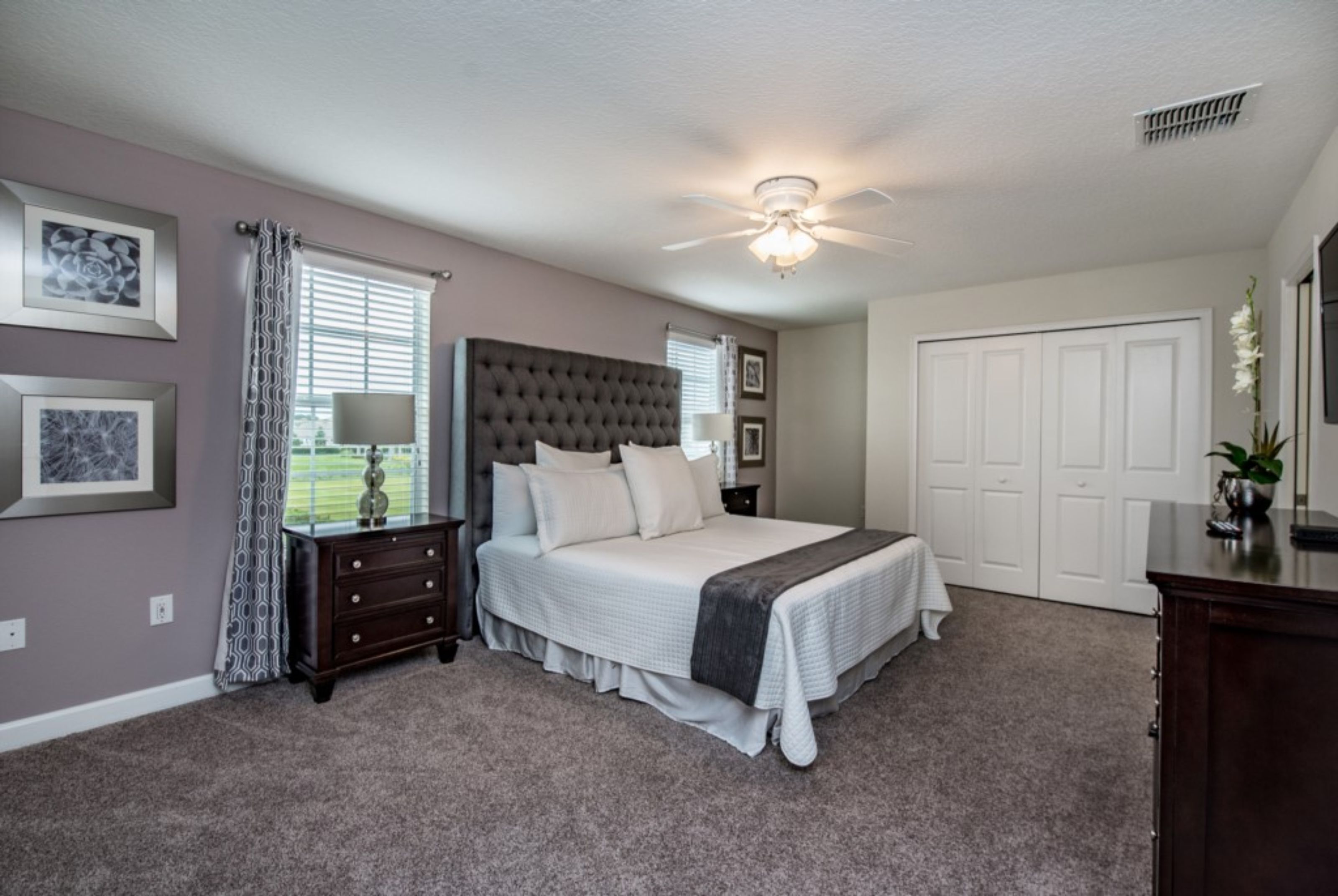 Une chambre à coucher avec un grand lit, un ventilateur de plafond, une commode et une fenêtre avec des rideaux.