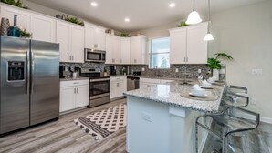 A modern kitchen with white cabinets, stainless steel appliances, granite countertops, and a central island with bar stools. - 9044st00 Premium-lot Location (Davenport)