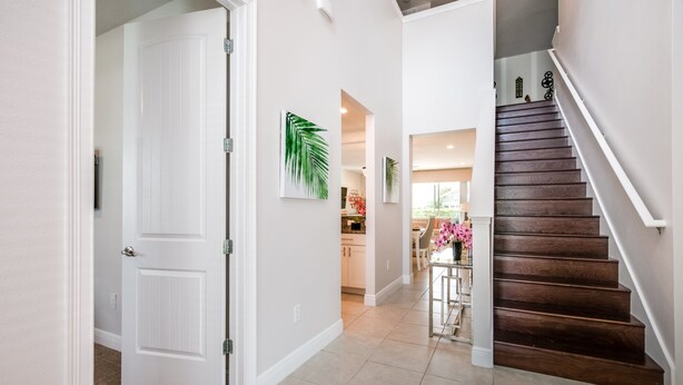 A hallway with a white door, a staircase, and a dining area with a table and chairs.
