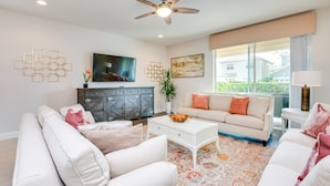 A modern living room with a ceiling fan, a flat-screen TV, a sofa, a coffee table, and a large window with a view.