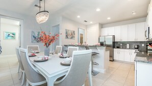 A modern kitchen with white cabinets, a stainless steel refrigerator, and a dining area with a white table and chairs.