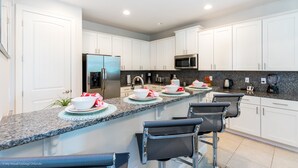 A modern kitchen with white cabinets, granite countertops, stainless steel appliances, and bar seating.