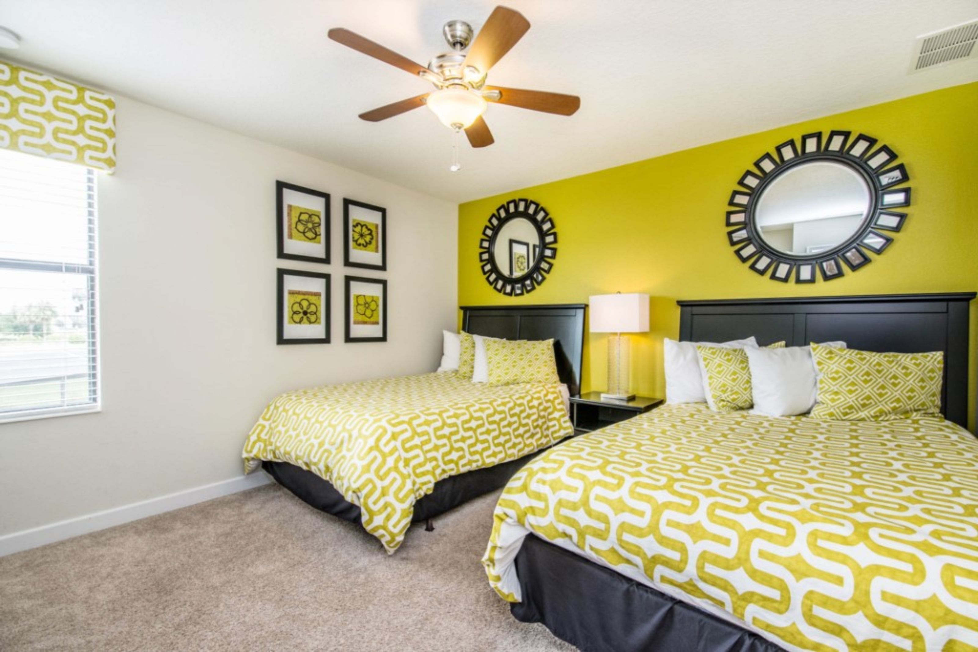 A hotel room with two beds, a ceiling fan, a large mirror, and framed artwork on the wall.