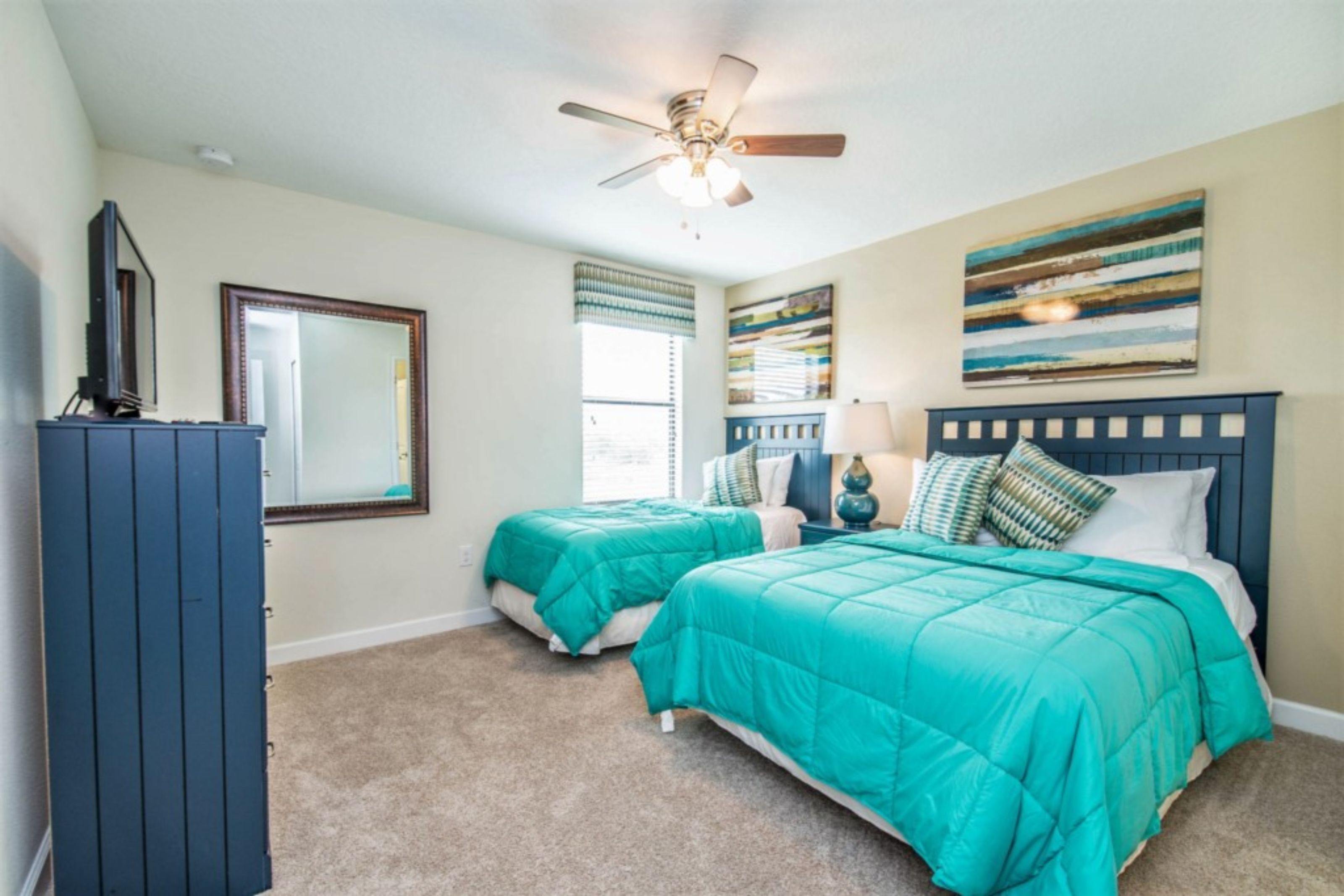 A bedroom with two beds, a ceiling fan, a dresser, and a large window with blinds.