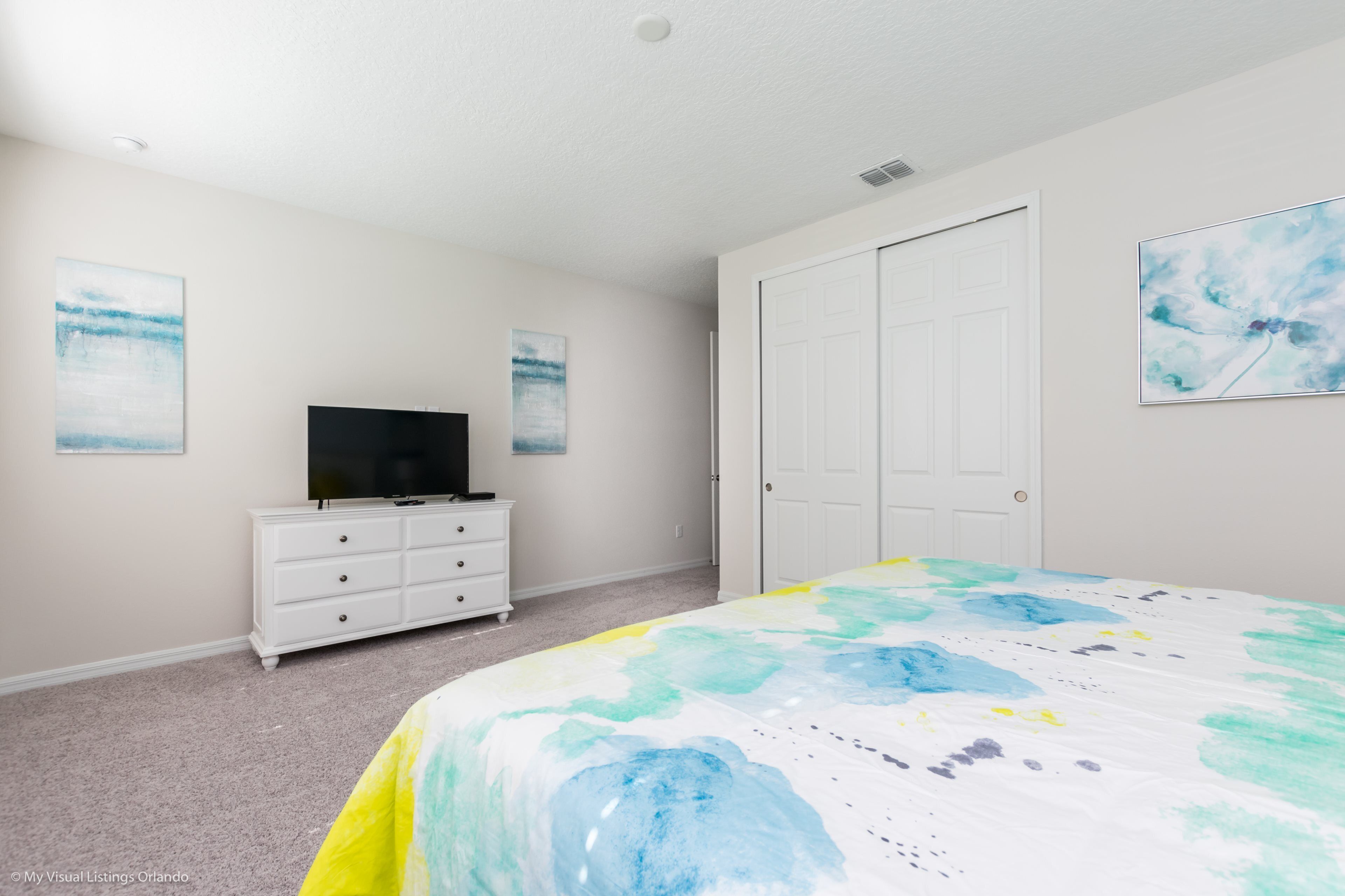 A bedroom with a bed, a dresser, a television, and two doors.