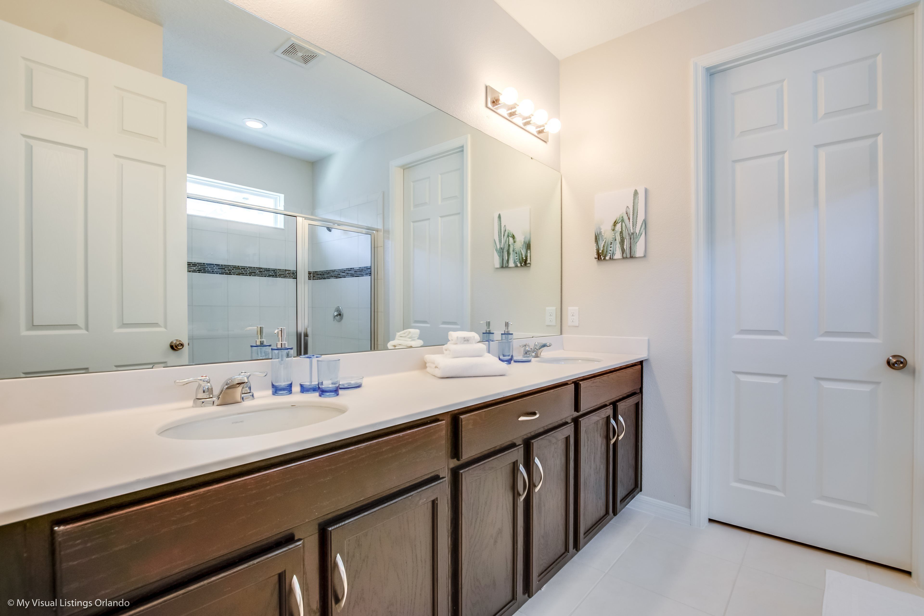 A modern bathroom with a large mirror, two sinks, and wooden cabinets.