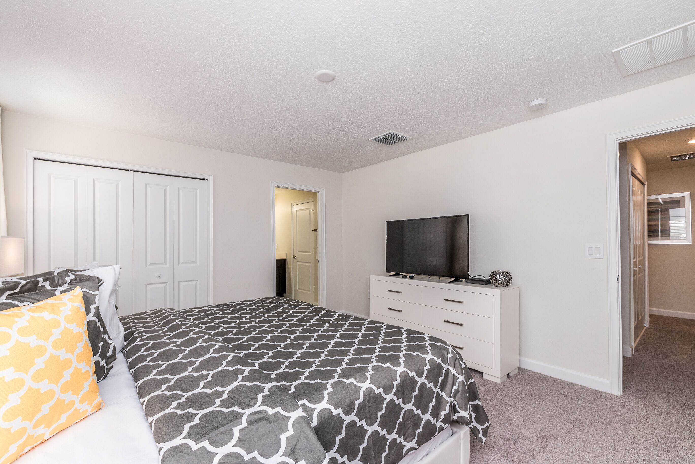 A bedroom with a bed, a dresser, a television, and a door leading to another room.