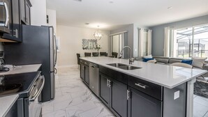 Una cucina moderna con mobili scuri, un'isola grande con un lavello e un'area pranzo illuminata da un lampadario.