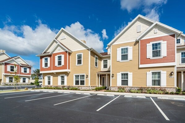 A row of modern, multi-story apartment buildings with a parking lot in front.