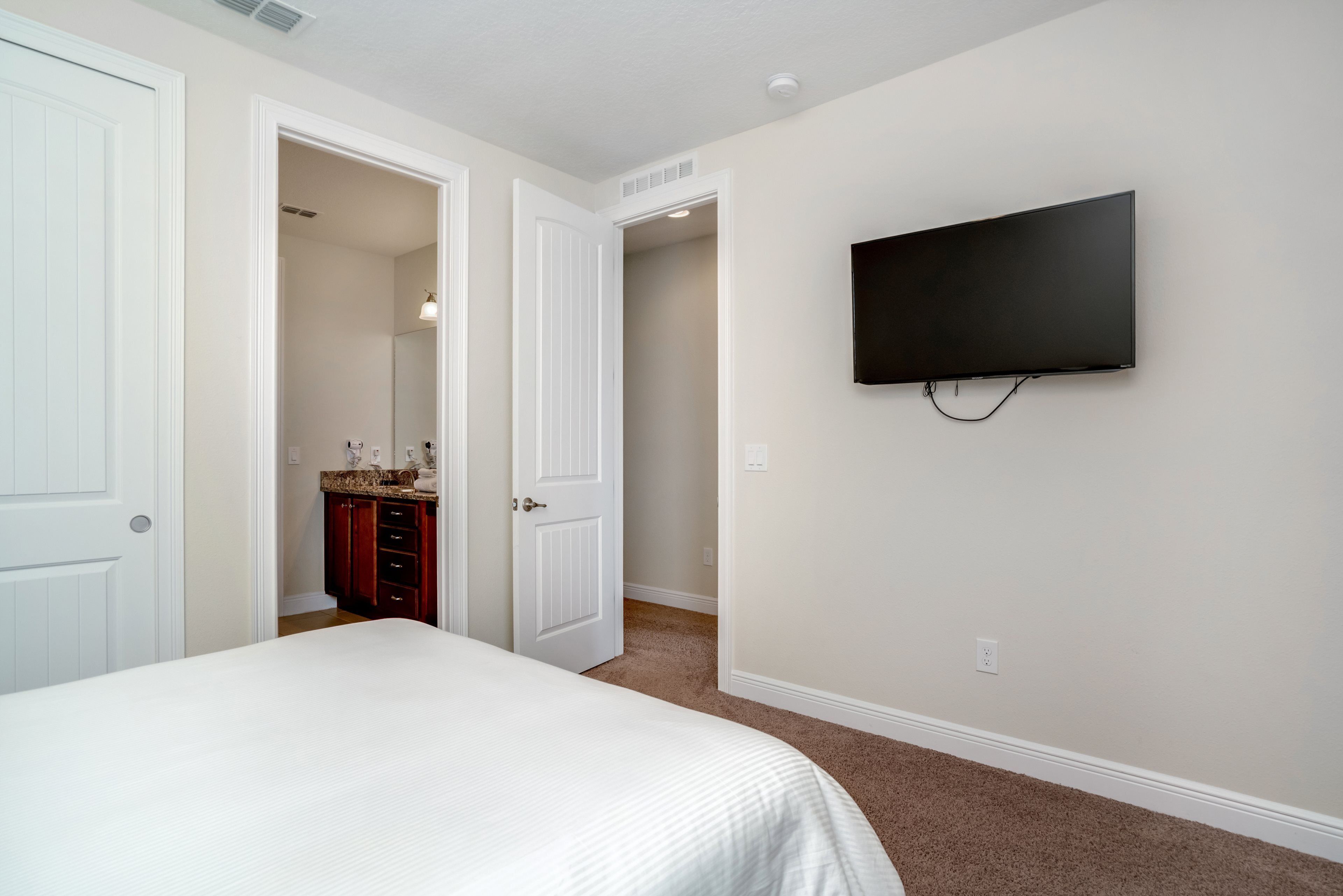 Ein Schlafzimmer mit einem Bett, einem an der Wand montierten Fernseher und einem durch eine offene Tür einsehbaren Badezimmer.