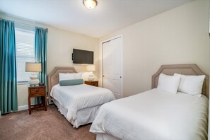 A hotel room with two beds, a TV mounted on the wall, a bedside table with a lamp, and a window with curtains. - Family Friendly 8 Bed Villa with Pool & Spa (Kissimmee)