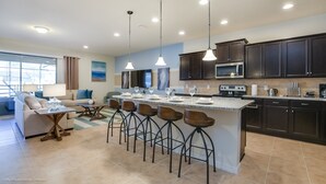 A modern kitchen with dark cabinets, a central island with stools, and a dining area with a sofa and table. - 9 Bed Villa with Games, Pool & Spa (Kissimmee)