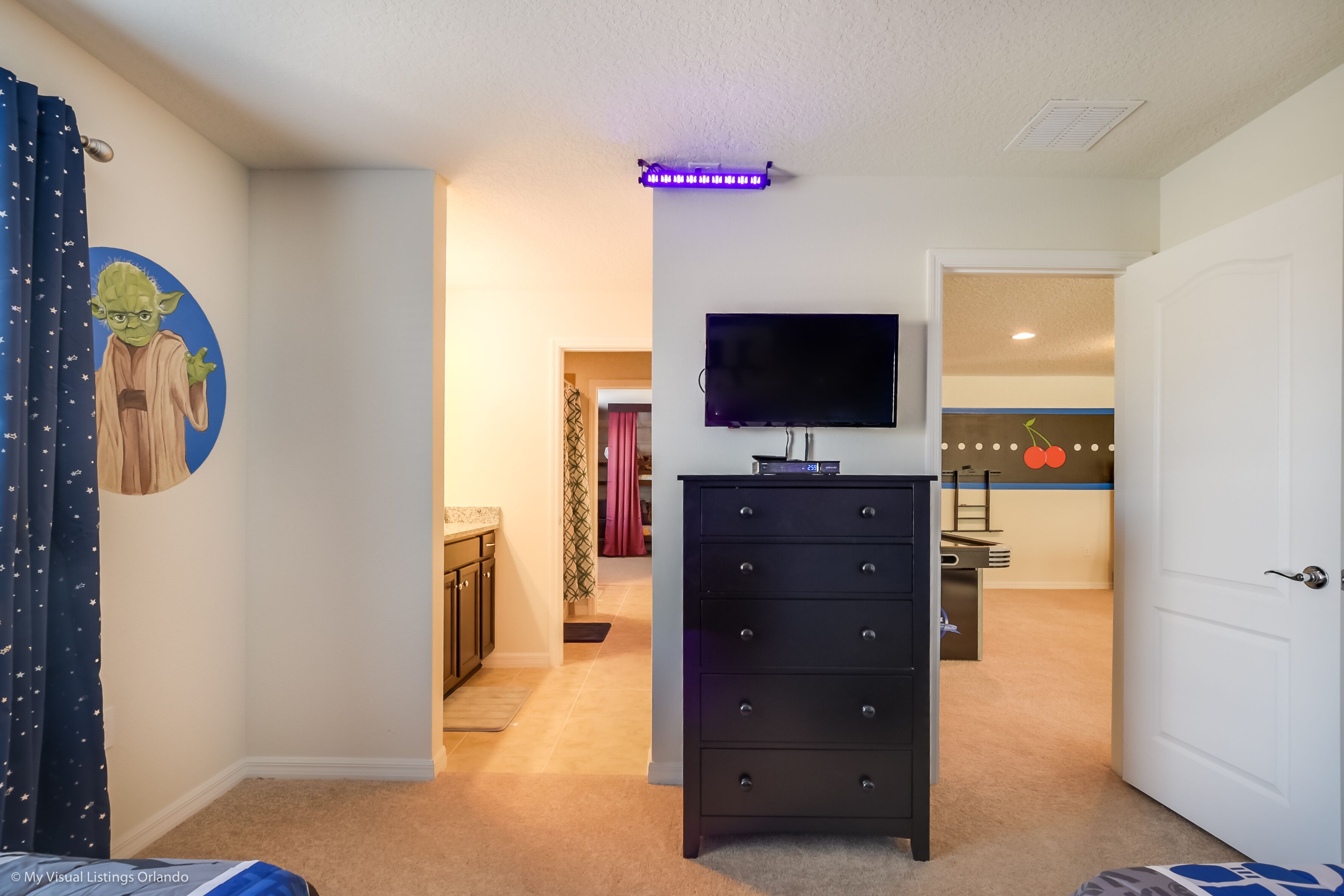 A bedroom with a TV on a dresser, a ceiling light, and a wall with a circular artwork.
