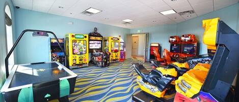 A room with a pool table, arcade games, and a racing simulator.
