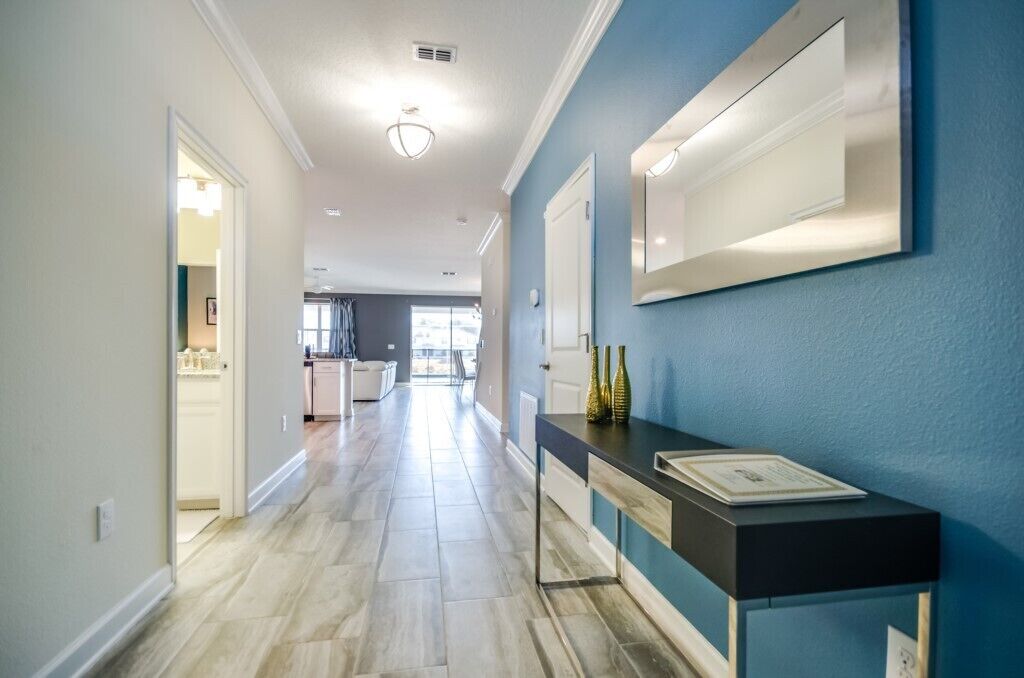 A hallway with a light-colored floor, a blue accent wall, and a black console table with bottles and a book.
