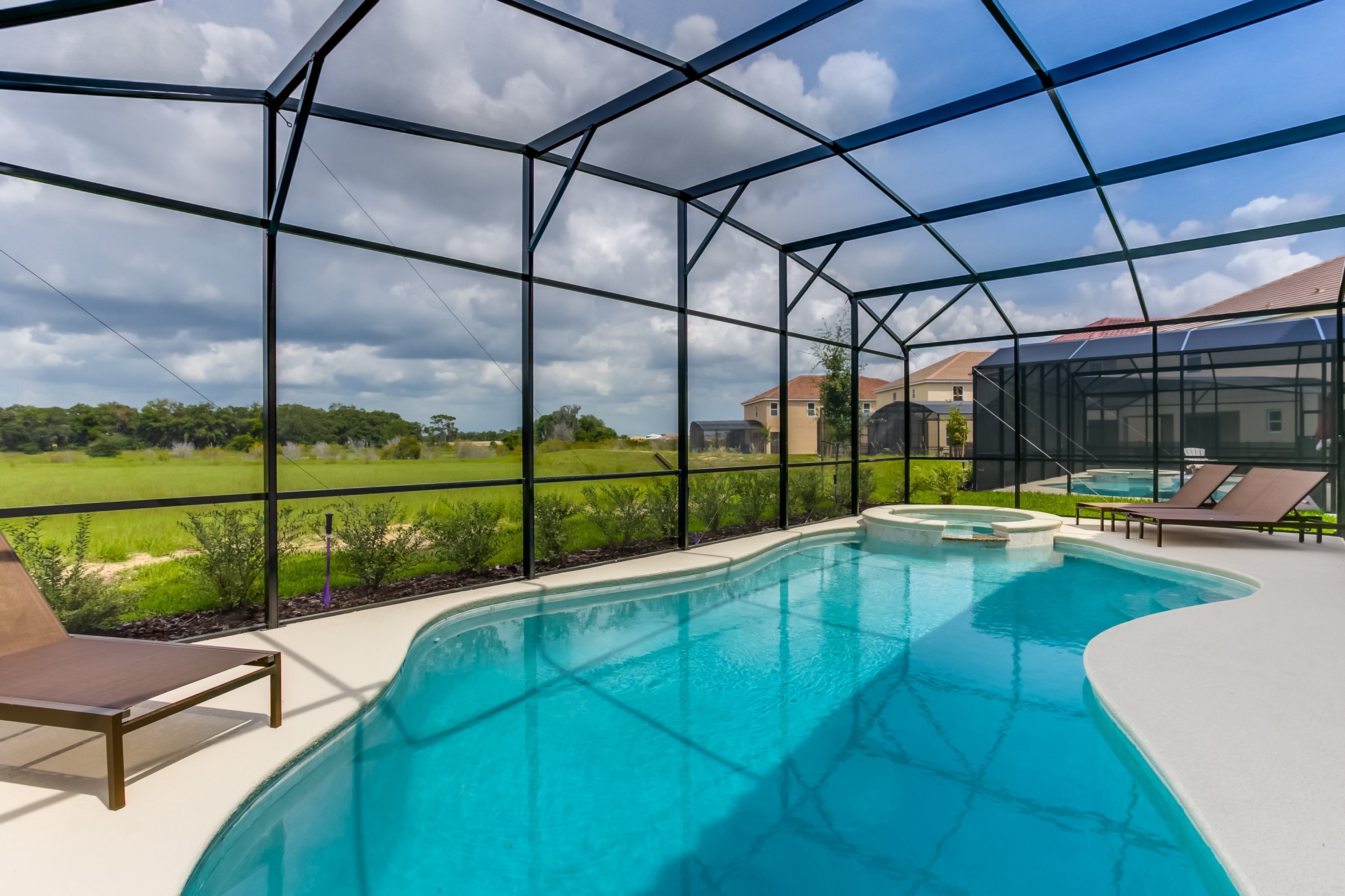 A swimming pool with a glass enclosure, surrounded by lounge chairs and a view of a green landscape.