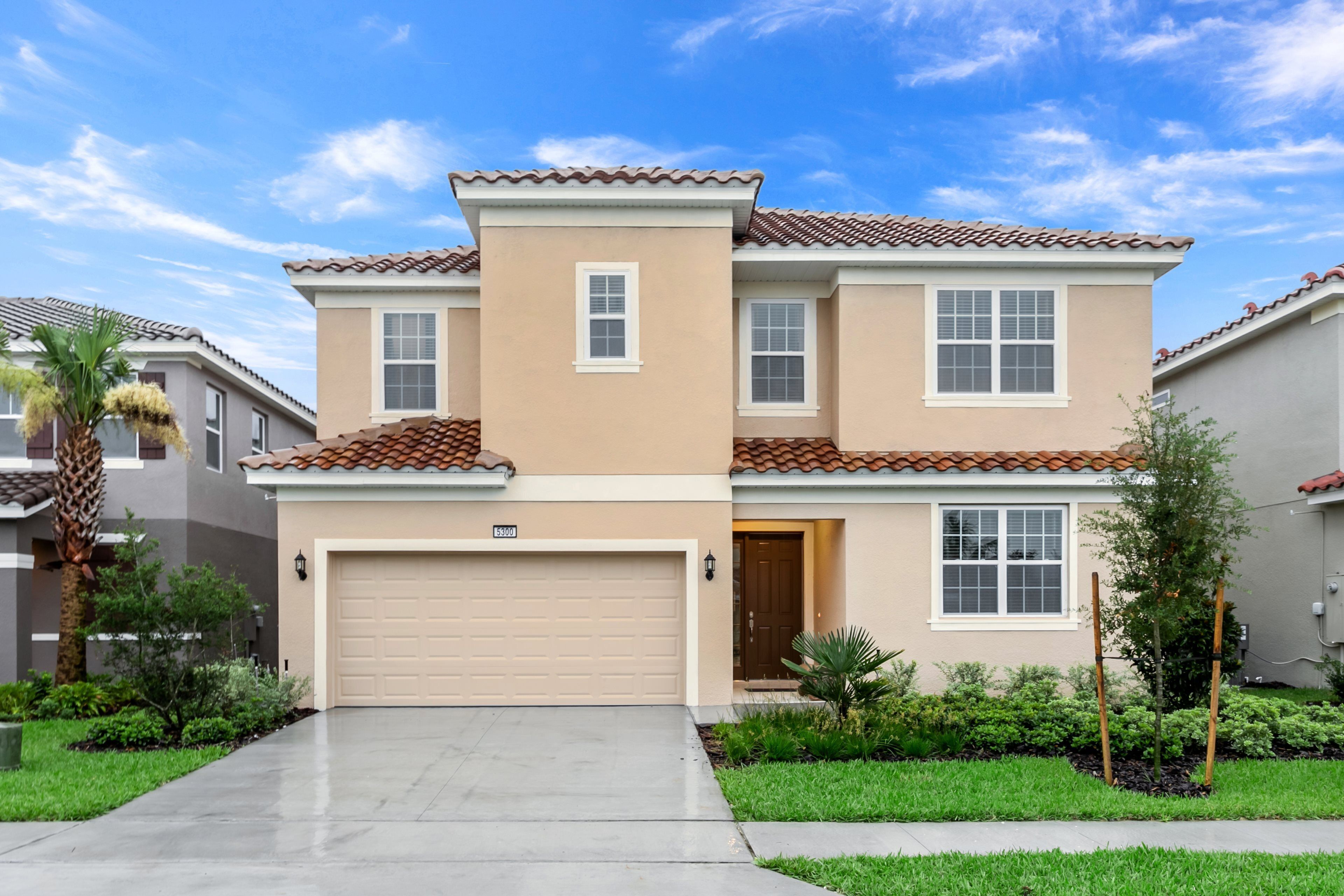 A two-story residential building with a beige facade, a tiled roof, and a garage.