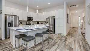 A modern kitchen with white cabinets, stainless steel appliances, and a central island with bar stools. - 5300oakb (Davenport)