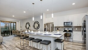 A modern kitchen with white cabinets, stainless steel appliances, and a central island with bar stools. - 5300oakb (Davenport)