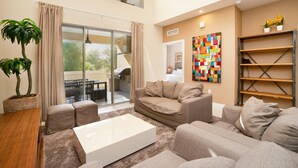 A modern living room with a sofa, a coffee table, a plant, and a colorful abstract painting on the wall. - New Magic Villa Resort Townhome 3123bra (Kissimmee)