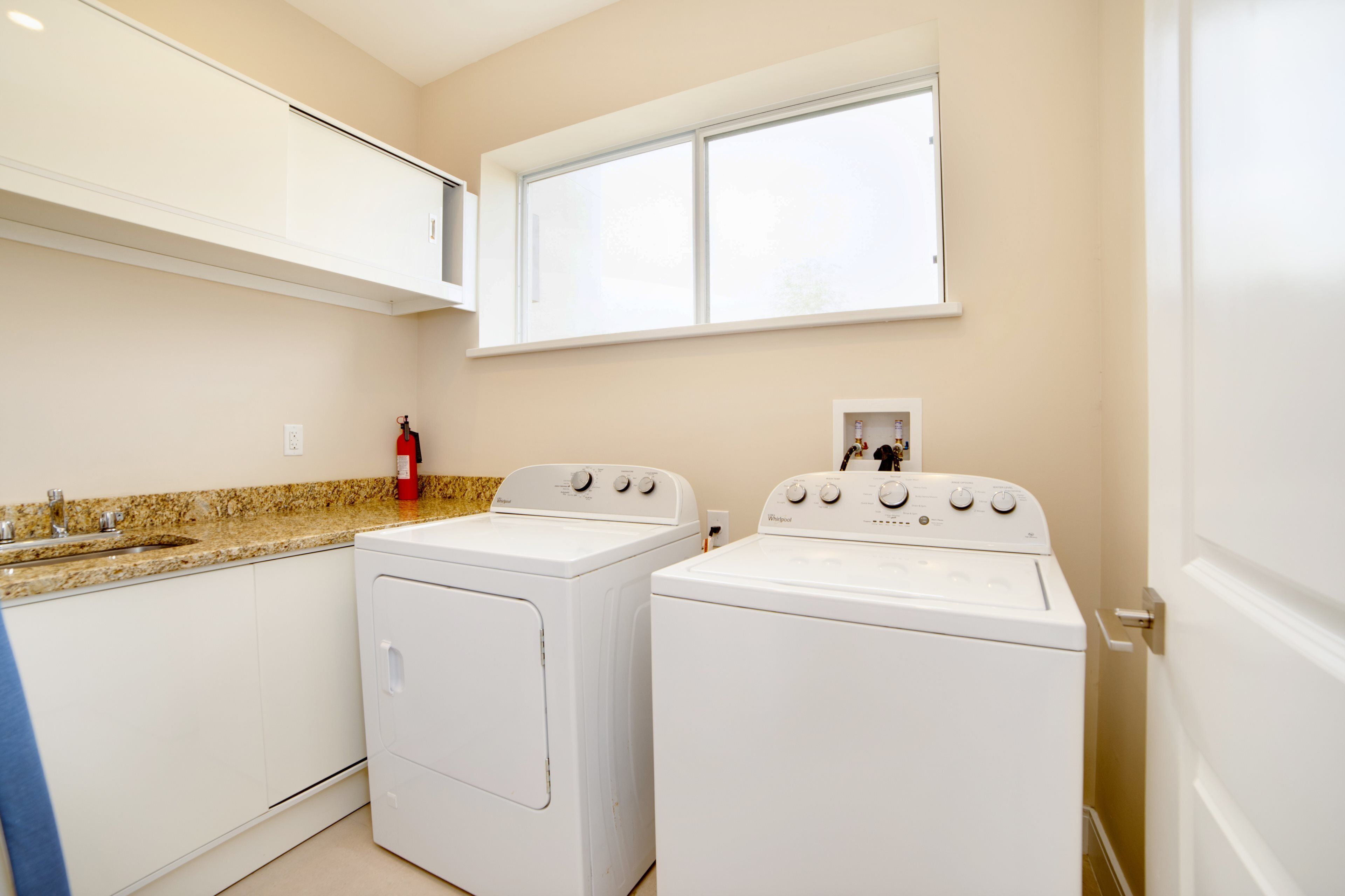 A laundry room with two white front-loading washers and a countertop with a sink.