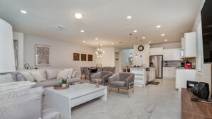 A modern living room with a sofa, armchairs, and a coffee table. There is a dining area with chairs and a table. The kitchen has white cabinets and stainless steel appliances. - 8 Bed 6 Ba Villa with Games, Pool & Spa (Kissimmee)