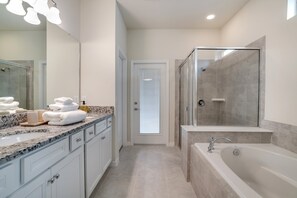 Un baño moderno con un espejo grande, una bañera, zona de ducha y tocador con encimera de mármol.