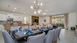 A modern dining area with a long table set for six, surrounded by grey upholstered chairs. - 8 Bed 6 Ba Villa with Games, Pool & Spa (Kissimmee)