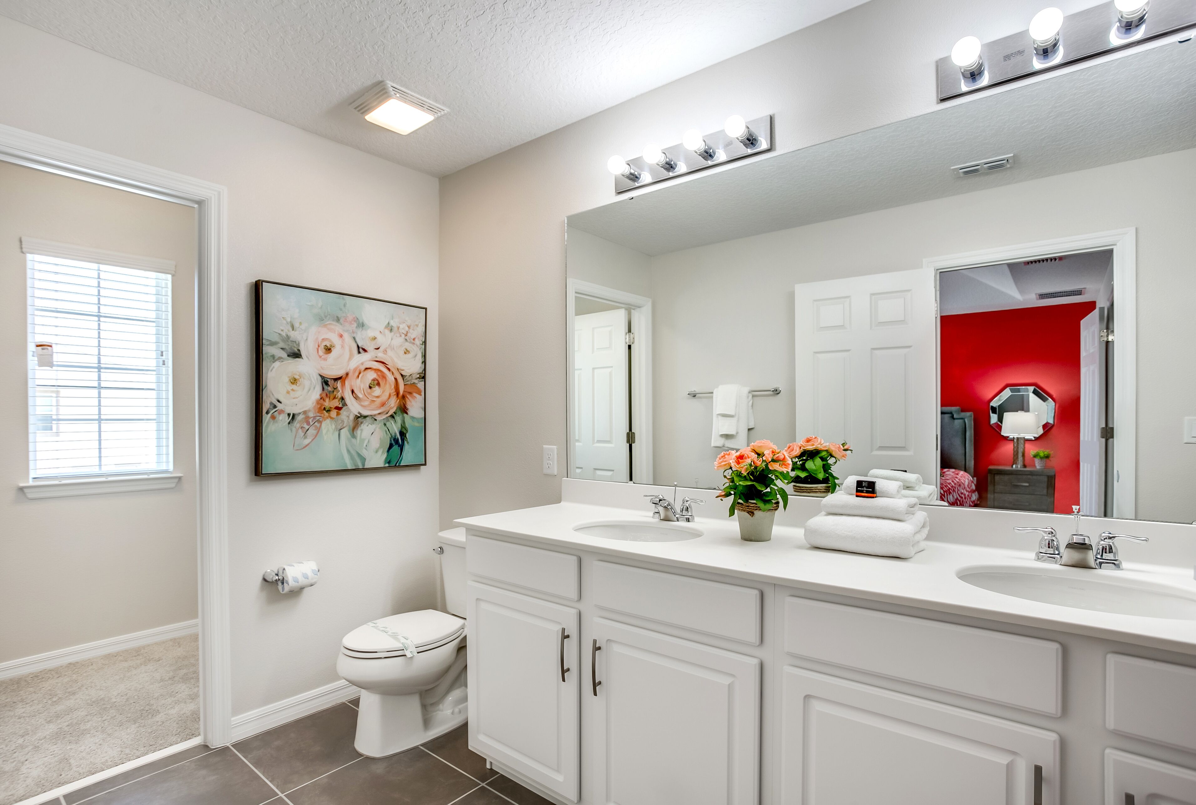A bathroom with a white vanity, a large mirror, and a floral painting on the wall.
