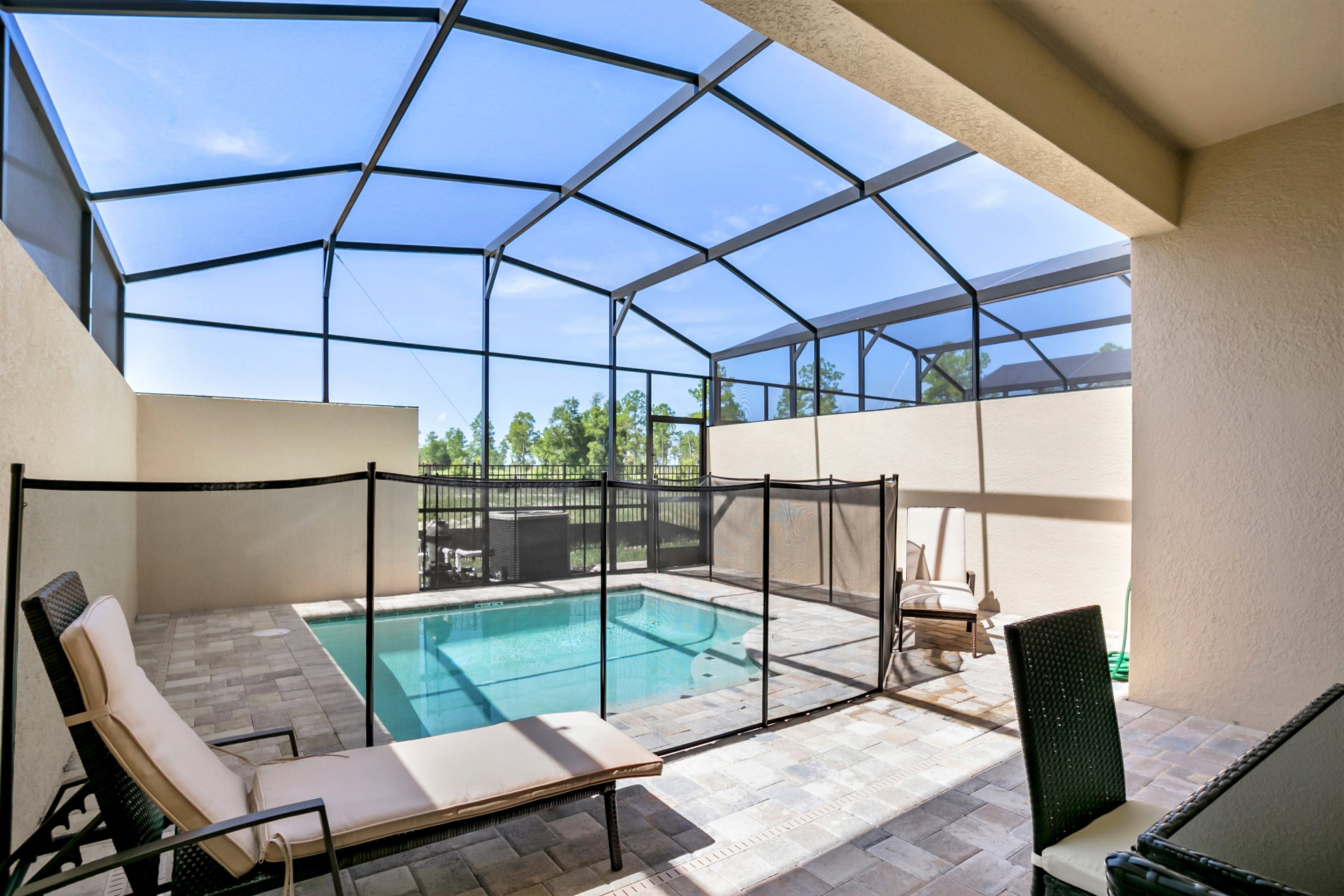 A covered outdoor swimming pool area with a glass enclosure, lounge chairs, and a patio table.