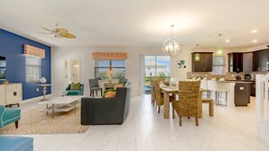 A modern open-plan living and dining area with a kitchen, featuring a ceiling fan, a dining table with chairs, and a kitchen island. - 9037hs 6 Bedroom 5 Bathroom Champions Gate Villa (Davenport)