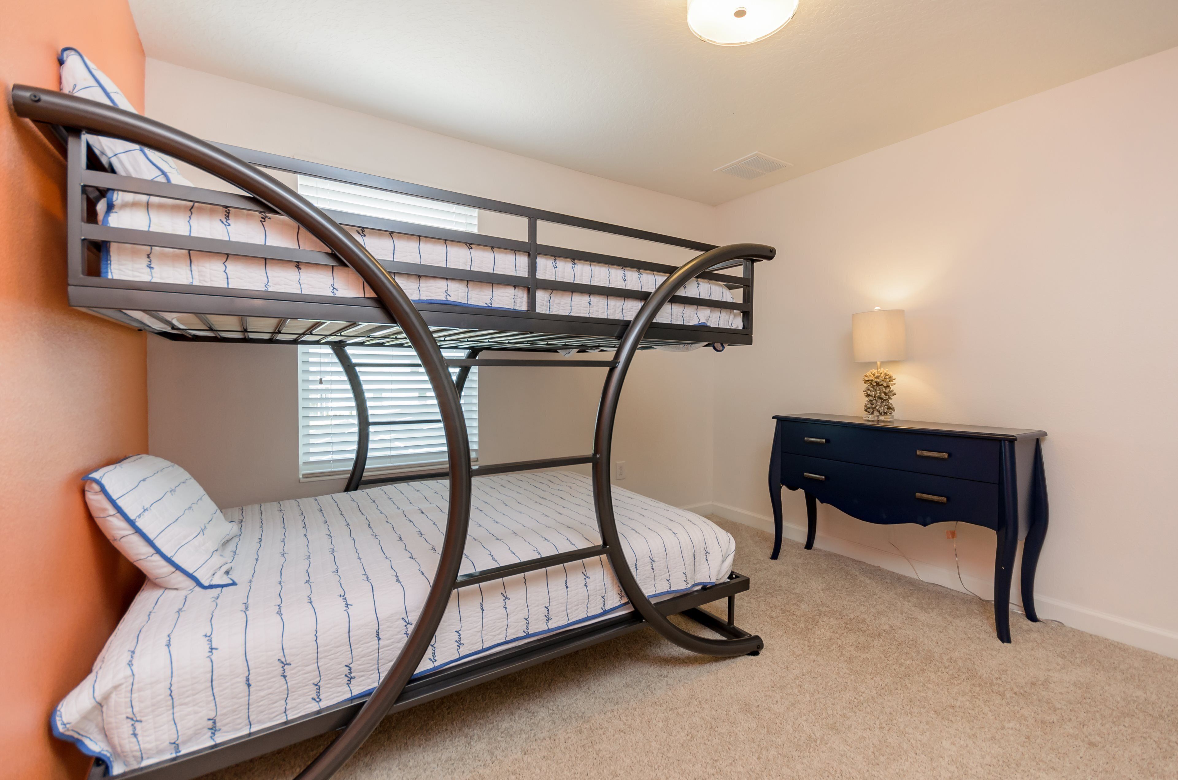 A bunk bed with a desk and lamp in a room with beige carpet and white walls.