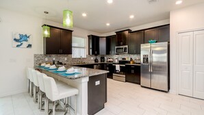 A modern kitchen with dark cabinets, stainless steel appliances, and a central island with bar stools. - 9037hs 6 Bedroom 5 Bathroom Champions Gate Villa (Davenport)