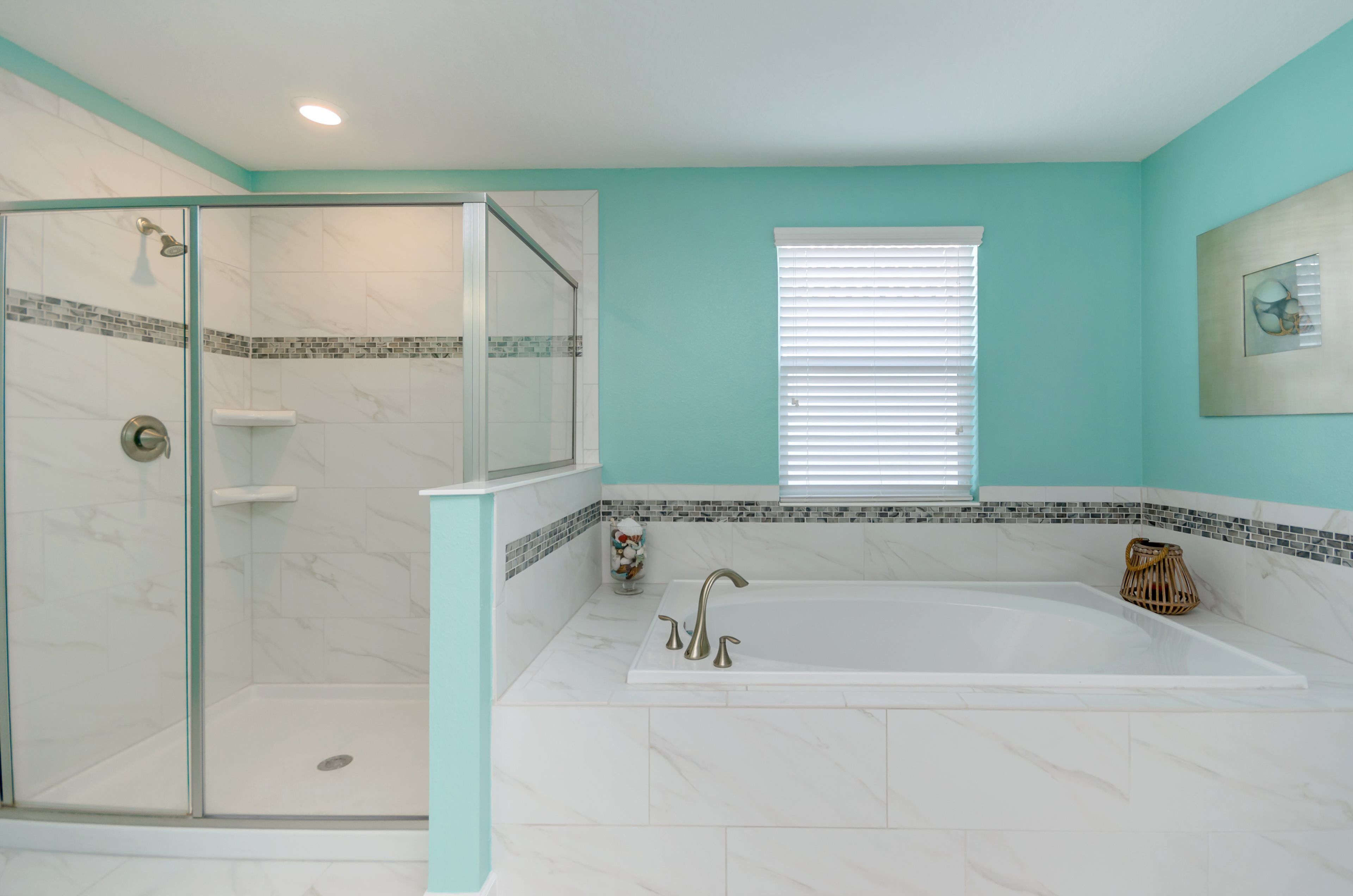 Une salle de bain dotée d’une douche à parois de verre, d’une baignoire sur pieds et d’une fenêtre avec des stores.