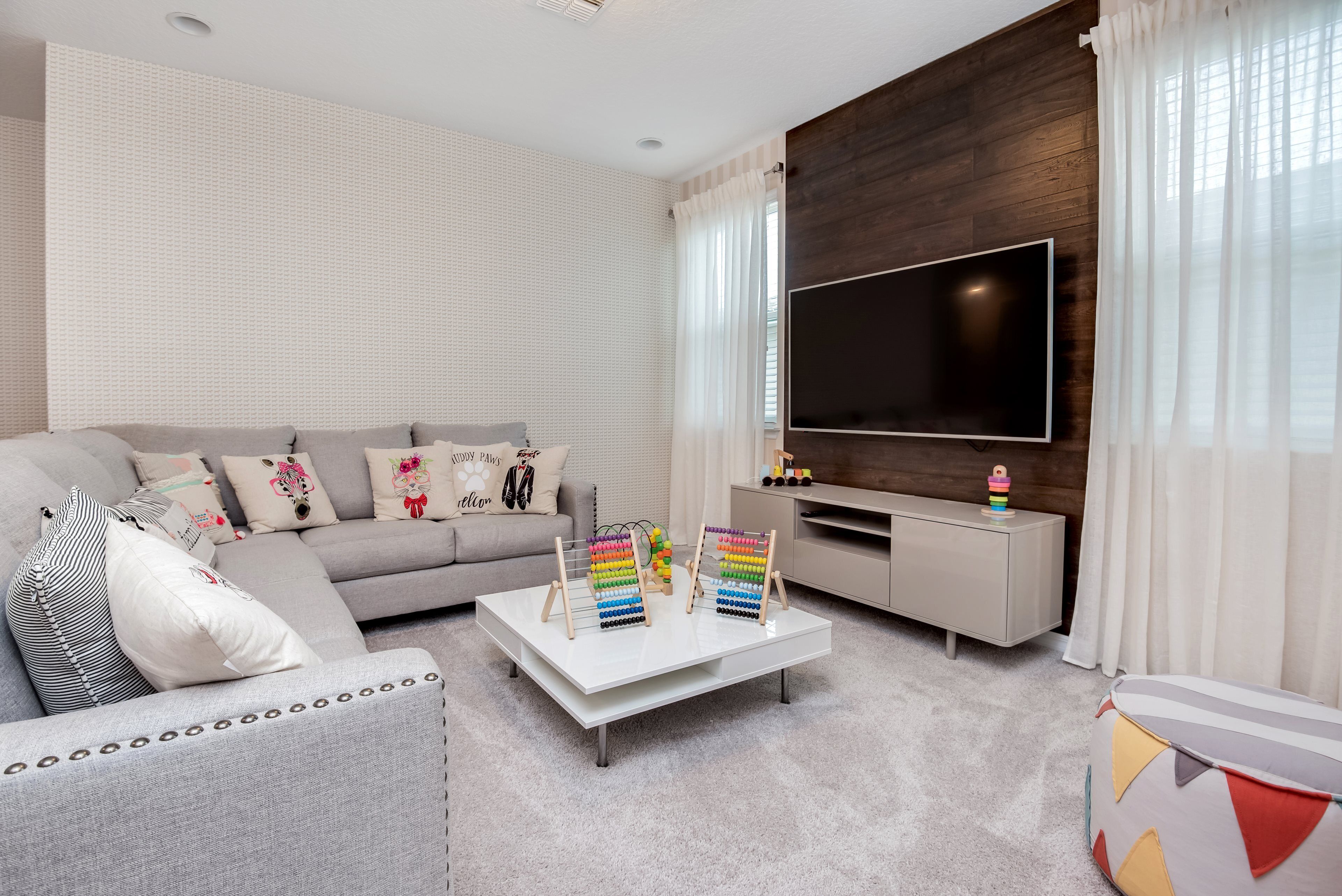 Un salon moderne avec un canapé gris, une table basse blanche et un téléviseur à écran plat.