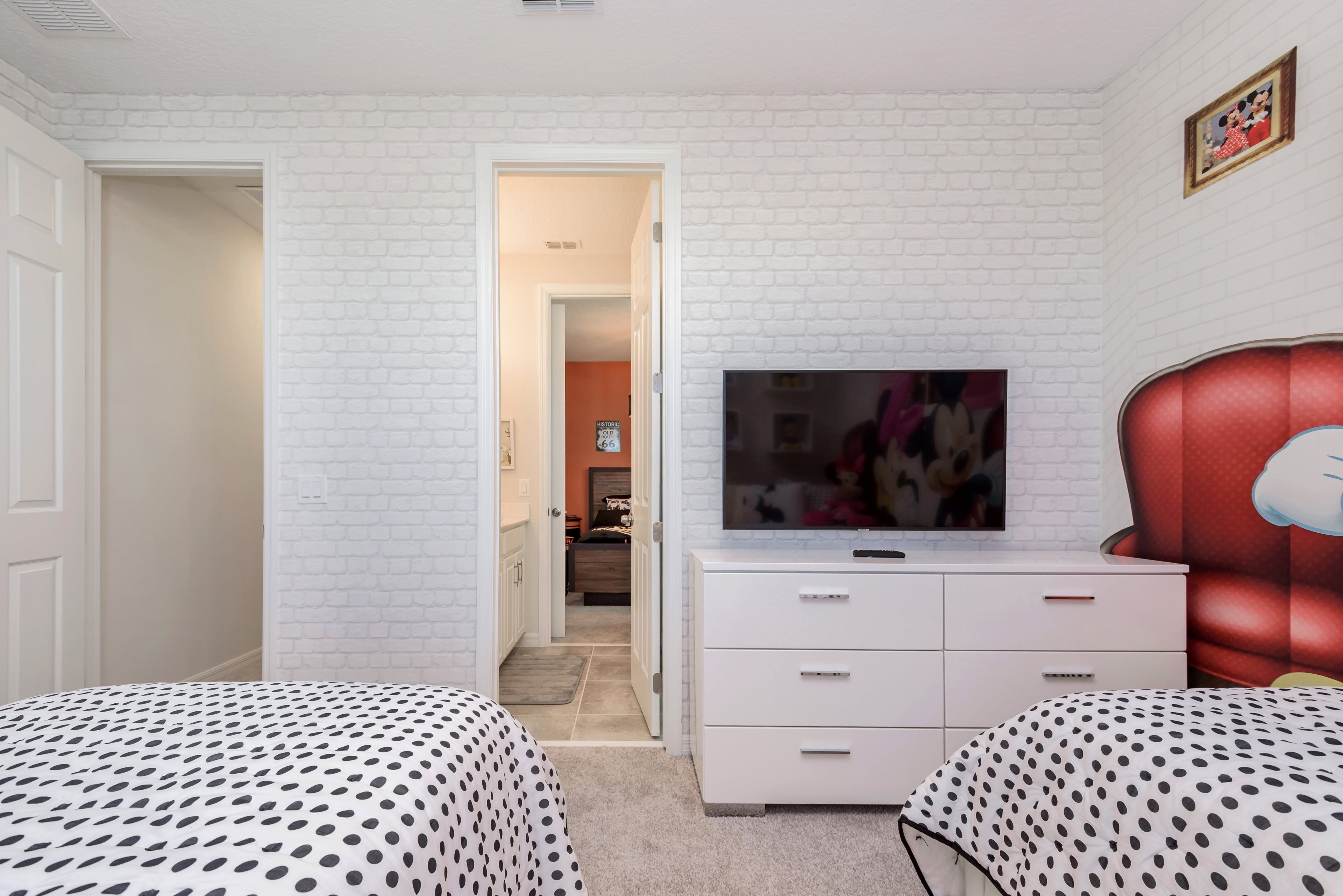 A bedroom with two beds, a TV, a dresser, and a red headboard.