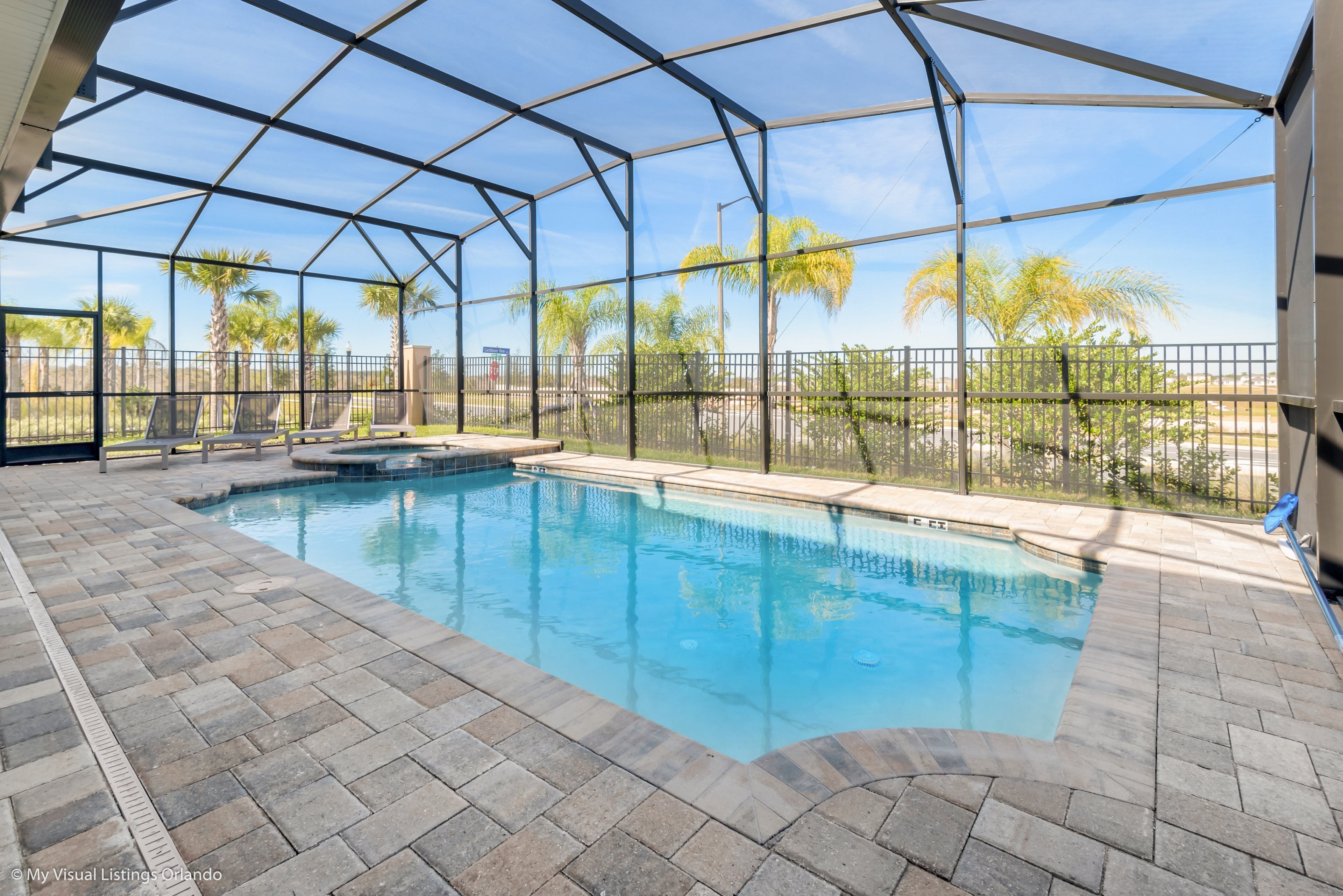 An indoor swimming pool with a clear view of palm trees and a fenced area.