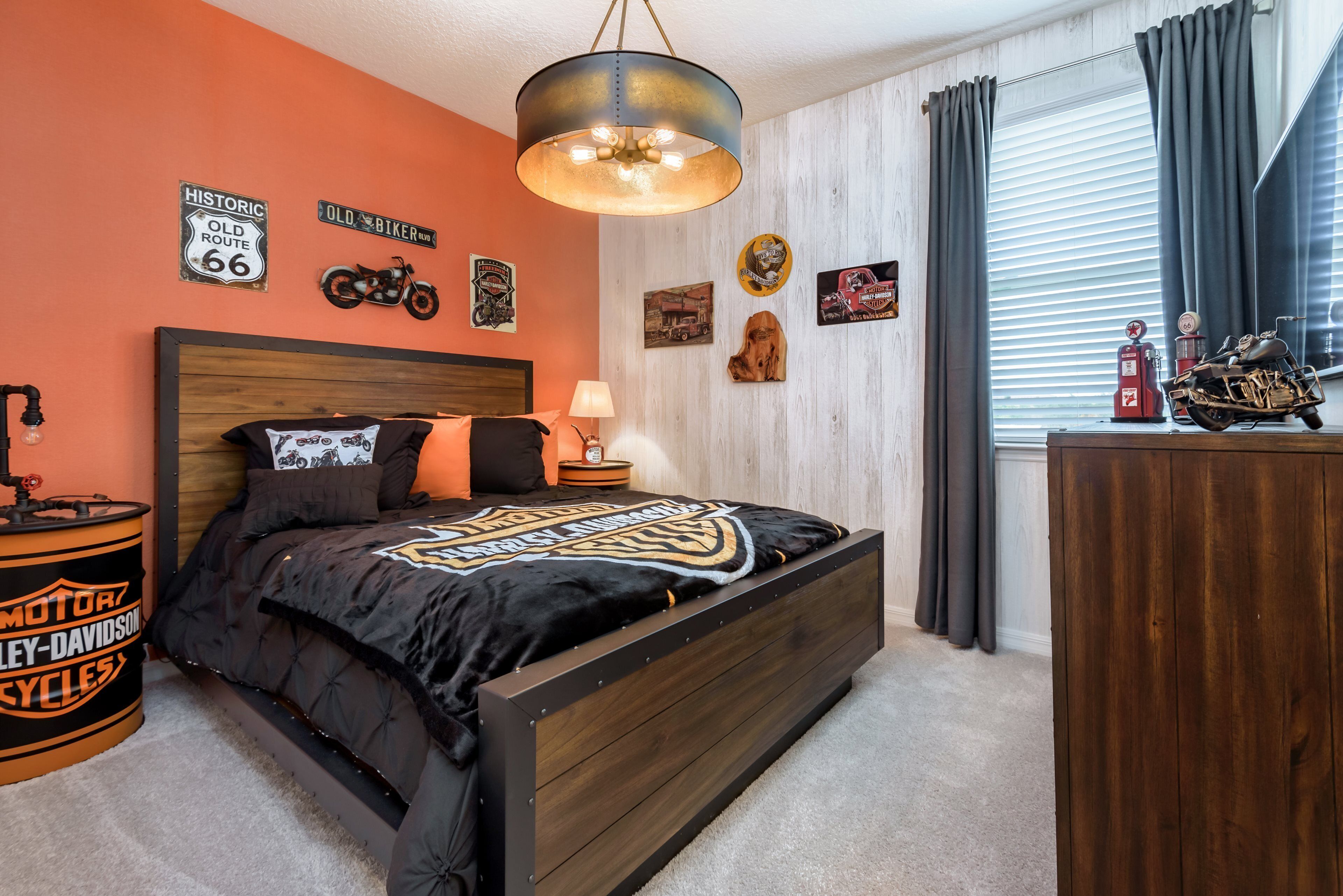A bedroom with a bed, a nightstand, a lamp, and wall decorations including signs and a motorcycle.