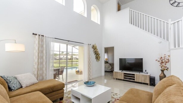 A spacious living room with a large TV, comfortable sofas, a staircase, and a view of the outdoors.