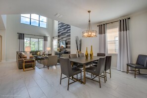 A spacious living room with a dining area, a high ceiling, and large windows.