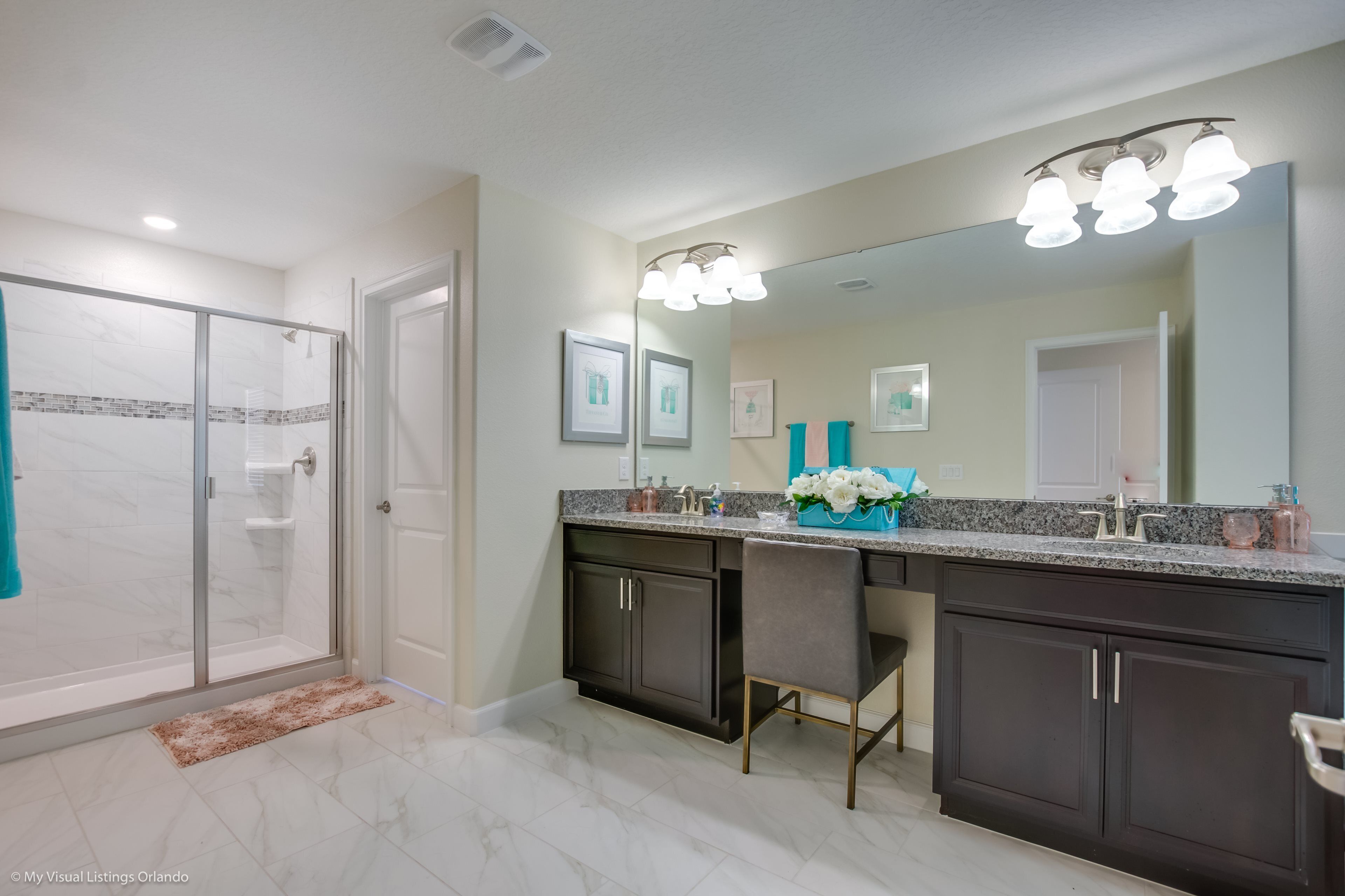 A modern bathroom with a glass shower enclosure, dark cabinetry, and a large vanity with a mirror.